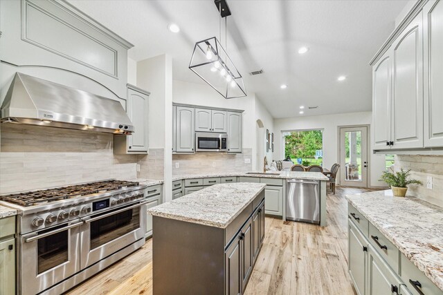 kitchen featuring pendant lighting, stainless steel appliances, light stone counters, and range hood