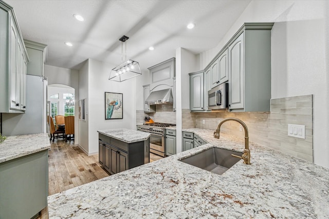 kitchen featuring light stone countertops, sink, stainless steel appliances, ventilation hood, and decorative light fixtures