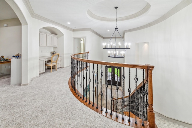 corridor featuring a notable chandelier, a raised ceiling, ornamental molding, and light carpet