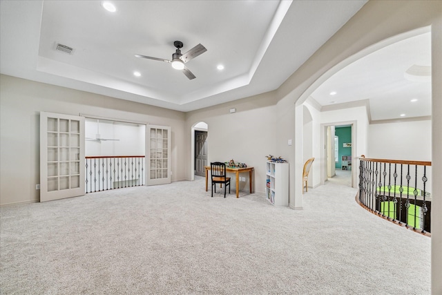 rec room with a raised ceiling, ceiling fan, french doors, and light carpet