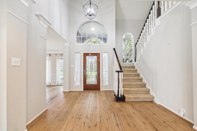 foyer entrance featuring light hardwood / wood-style floors, a towering ceiling, and an inviting chandelier