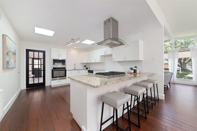 kitchen featuring a kitchen bar, kitchen peninsula, white cabinetry, stainless steel appliances, and island range hood