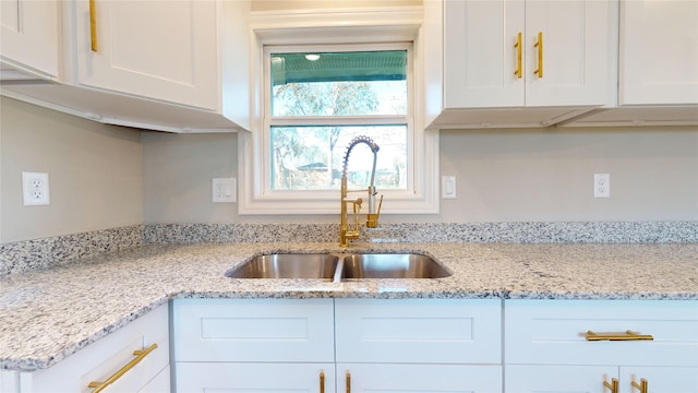 kitchen with light stone counters, sink, and white cabinets