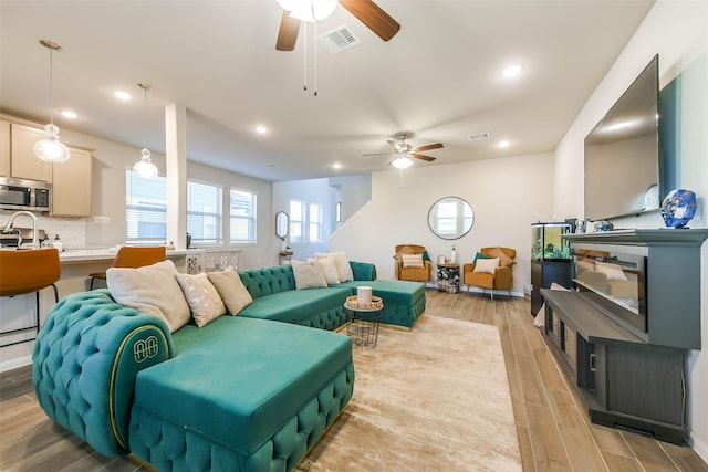 living room featuring ceiling fan, sink, and light wood-type flooring