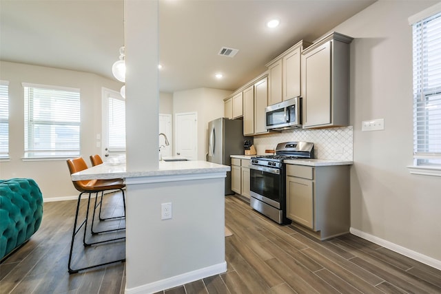 kitchen featuring a kitchen breakfast bar, sink, decorative backsplash, gray cabinets, and stainless steel appliances