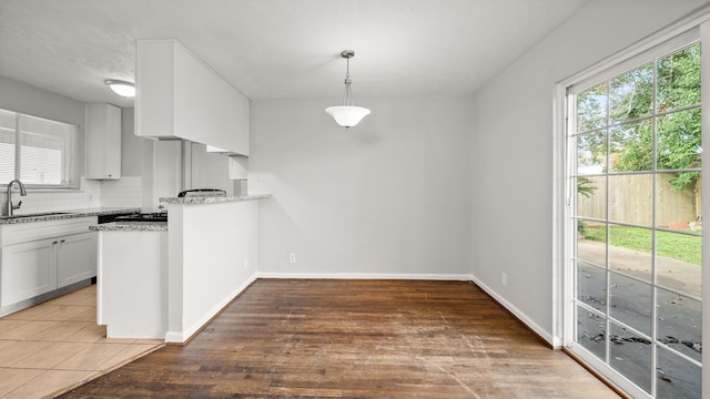 kitchen featuring white cabinets, sink, hanging light fixtures, decorative backsplash, and light stone counters