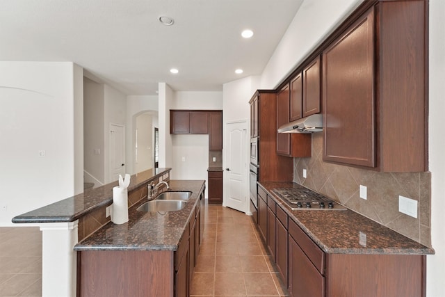 kitchen with backsplash, a center island with sink, sink, dark stone countertops, and appliances with stainless steel finishes