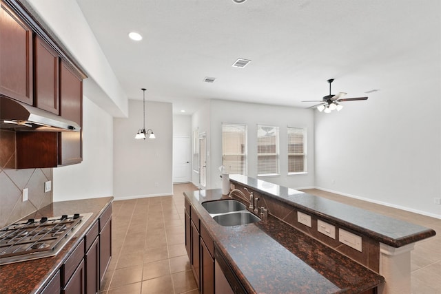 kitchen featuring sink, stainless steel gas cooktop, backsplash, decorative light fixtures, and ceiling fan with notable chandelier