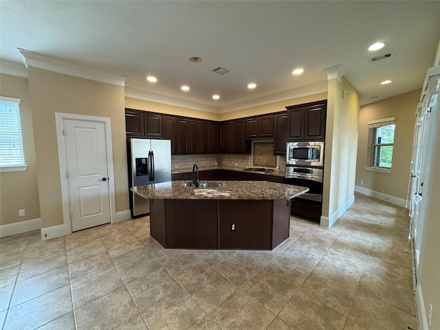 kitchen featuring stainless steel appliances, an island with sink, backsplash, dark stone counters, and sink