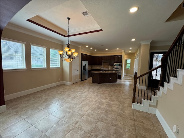 kitchen with stainless steel appliances, a raised ceiling, a notable chandelier, tasteful backsplash, and a kitchen island