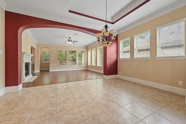 empty room with a tray ceiling, crown molding, ceiling fan with notable chandelier, and light tile patterned floors