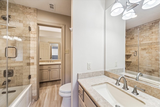 full bathroom with toilet, bath / shower combo with glass door, a textured ceiling, vanity, and hardwood / wood-style floors