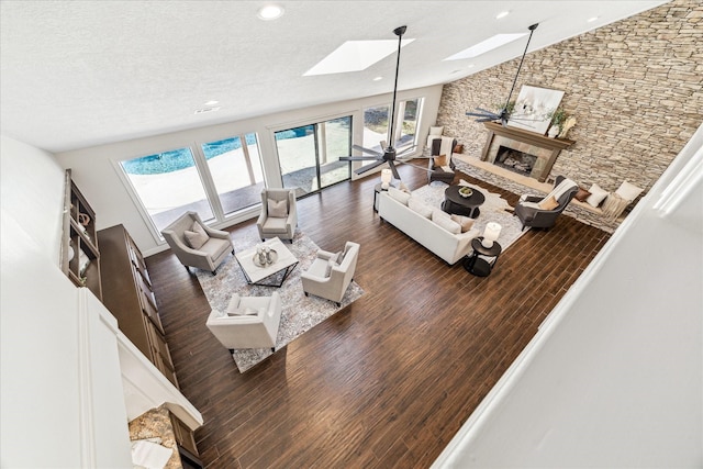 living room featuring a stone fireplace, a skylight, high vaulted ceiling, dark hardwood / wood-style flooring, and ceiling fan