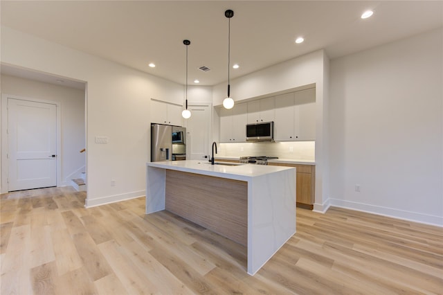 kitchen featuring an island with sink, sink, white cabinets, hanging light fixtures, and stainless steel appliances