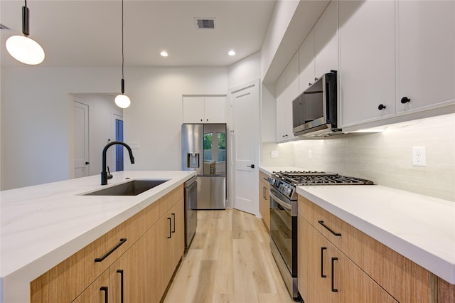 kitchen featuring stainless steel appliances, white cabinetry, sink, and pendant lighting