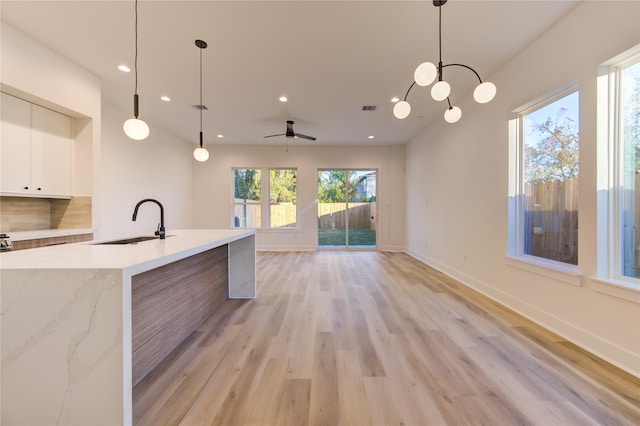 kitchen featuring sink, light stone counters, decorative light fixtures, light wood-type flooring, and white cabinets