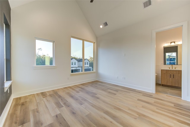 unfurnished bedroom with ensuite bathroom, sink, high vaulted ceiling, and light hardwood / wood-style flooring