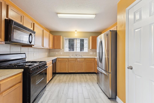 kitchen with light brown cabinets, backsplash, black appliances, sink, and light wood-type flooring