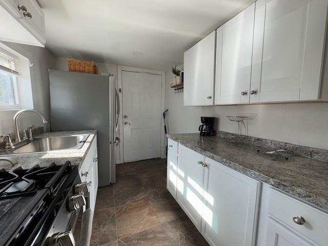 kitchen featuring white cabinets, stainless steel gas range, dark stone counters, and sink