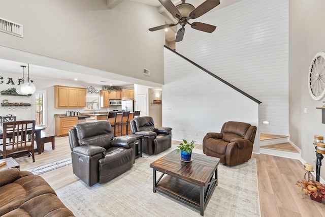 living room featuring ceiling fan, light hardwood / wood-style floors, and a high ceiling