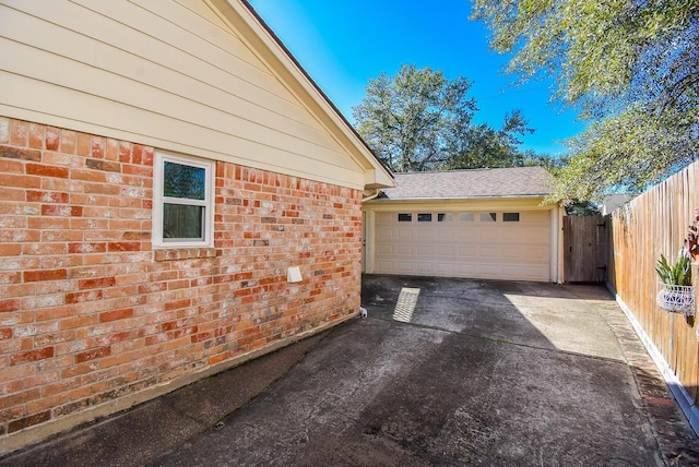 view of home's exterior with concrete driveway, brick siding, an attached garage, and fence