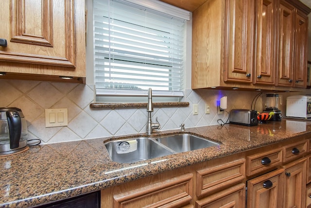 kitchen with black dishwasher, tasteful backsplash, a sink, and brown cabinets