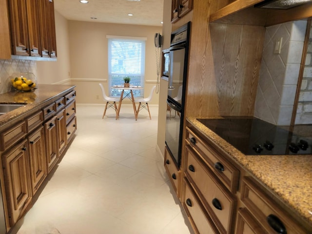 kitchen featuring brown cabinets, tasteful backsplash, light stone counters, and black electric cooktop