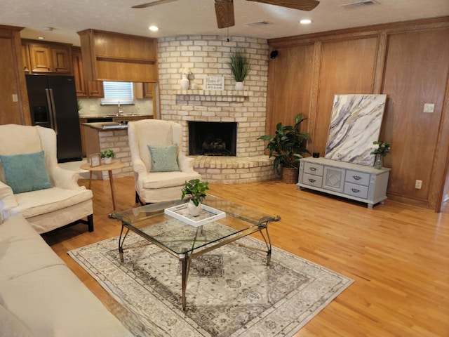 living room with light wood-style floors, ceiling fan, a brick fireplace, and a textured ceiling