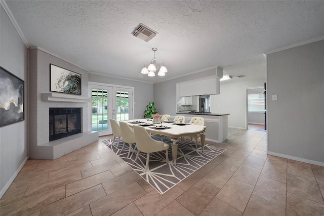 tiled dining area with french doors, a brick fireplace, a textured ceiling, crown molding, and a notable chandelier