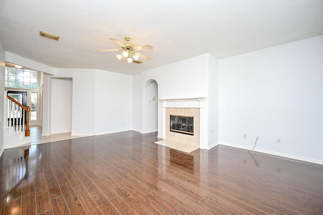 unfurnished living room featuring a tiled fireplace, ceiling fan, dark hardwood / wood-style flooring, and a textured ceiling