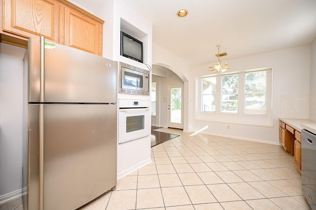 kitchen with light brown cabinets, light tile patterned floors, appliances with stainless steel finishes, and an inviting chandelier