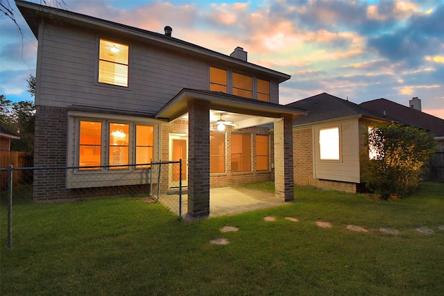 back house at dusk with a lawn and a patio area