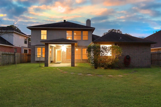 back house at dusk with a lawn and a patio area