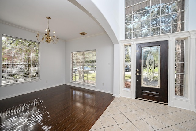 entryway with light tile patterned floors, ornamental molding, and an inviting chandelier