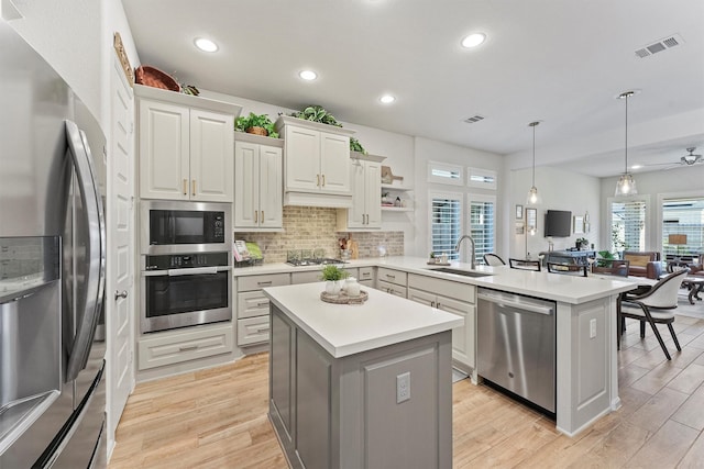 kitchen with kitchen peninsula, stainless steel appliances, sink, a center island, and hanging light fixtures