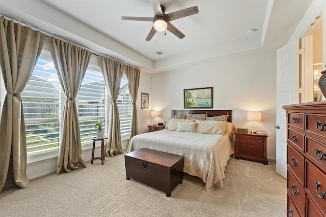 bedroom featuring light carpet, multiple windows, a tray ceiling, and ceiling fan