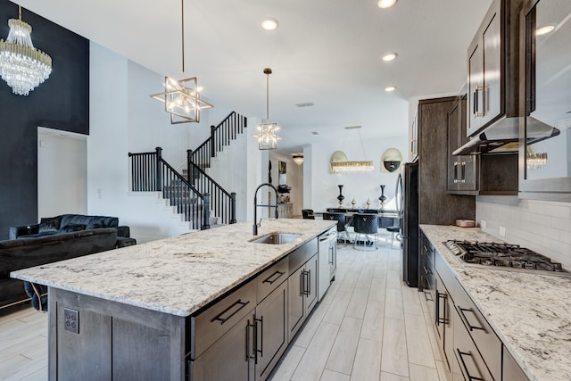 kitchen featuring appliances with stainless steel finishes, light stone counters, a kitchen island with sink, sink, and pendant lighting