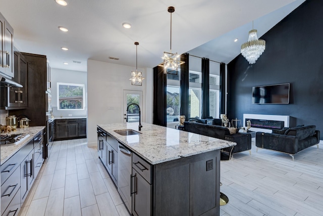 kitchen with light stone countertops, appliances with stainless steel finishes, a kitchen island with sink, sink, and pendant lighting