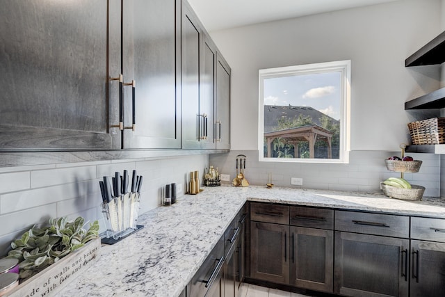 kitchen with light stone counters, tasteful backsplash, open shelves, and dark brown cabinetry