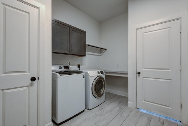laundry room featuring baseboards, light wood-type flooring, cabinet space, and washing machine and dryer