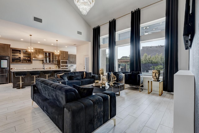living area featuring light wood finished floors, visible vents, high vaulted ceiling, and ceiling fan with notable chandelier