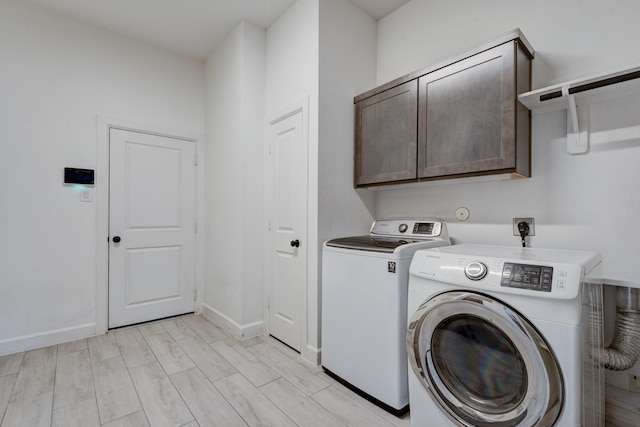 clothes washing area featuring baseboards, washer and dryer, and cabinet space