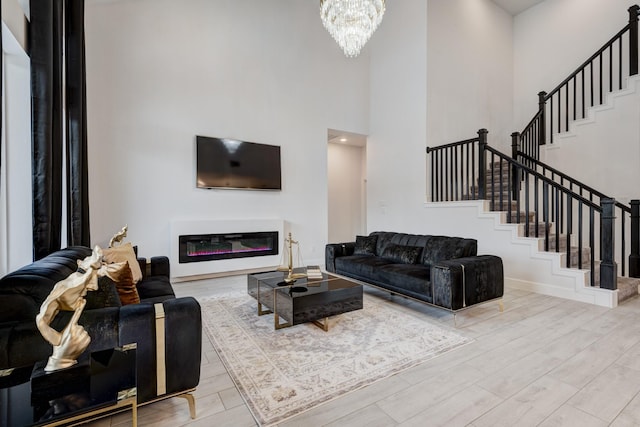 living area featuring stairway, an inviting chandelier, a glass covered fireplace, wood finished floors, and a high ceiling