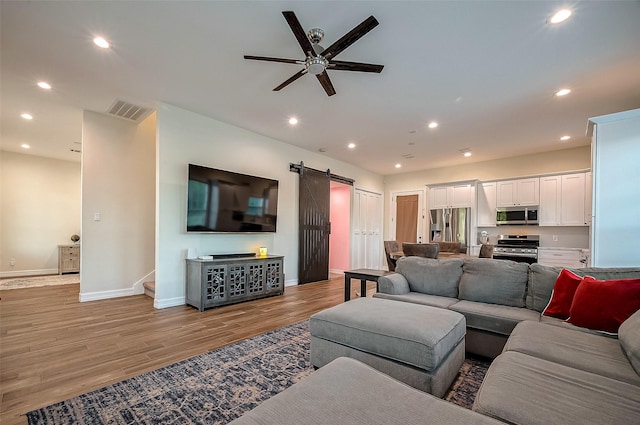 living room featuring ceiling fan, a barn door, and light wood-type flooring