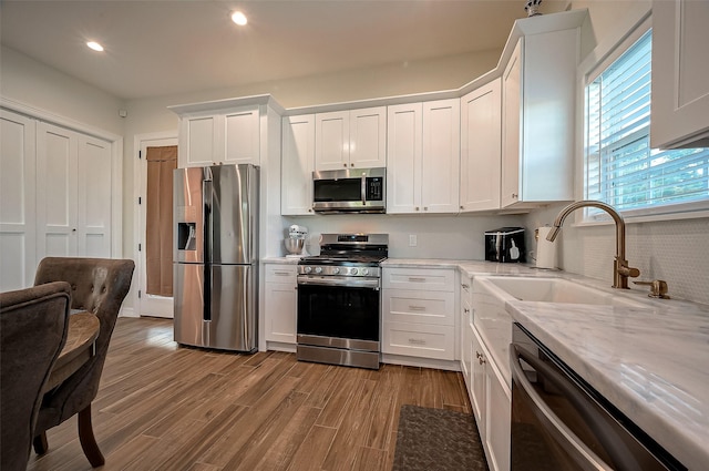 kitchen with sink, light stone countertops, appliances with stainless steel finishes, light hardwood / wood-style floors, and white cabinetry