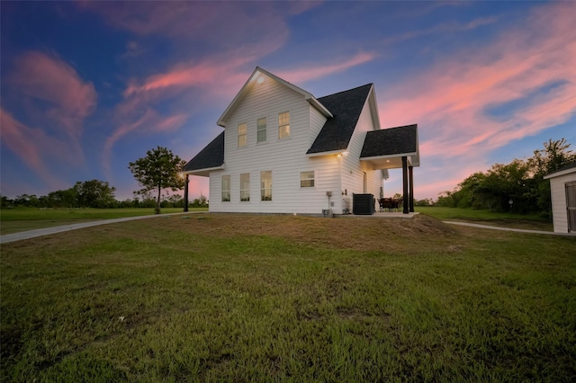 back house at dusk featuring a lawn and central air condition unit