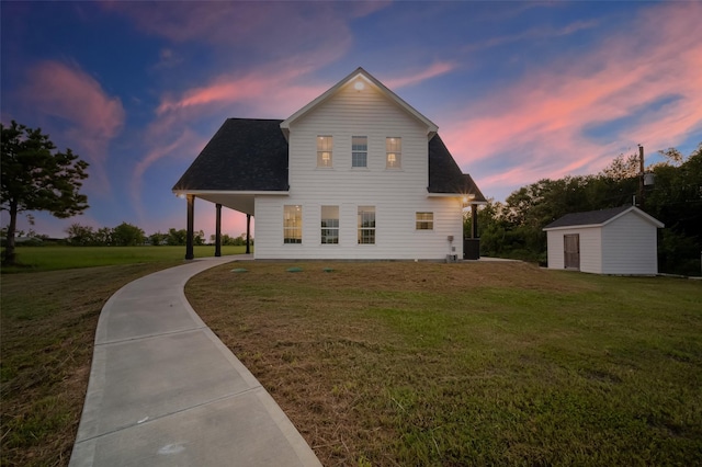 back house at dusk featuring a yard and a storage unit