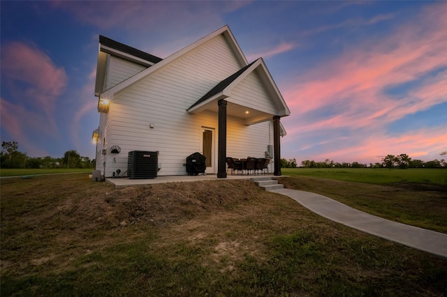 back house at dusk with central AC unit, a yard, and a patio