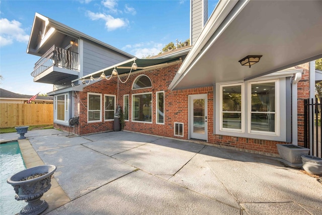 rear view of property featuring a patio area, a balcony, and a fenced in pool