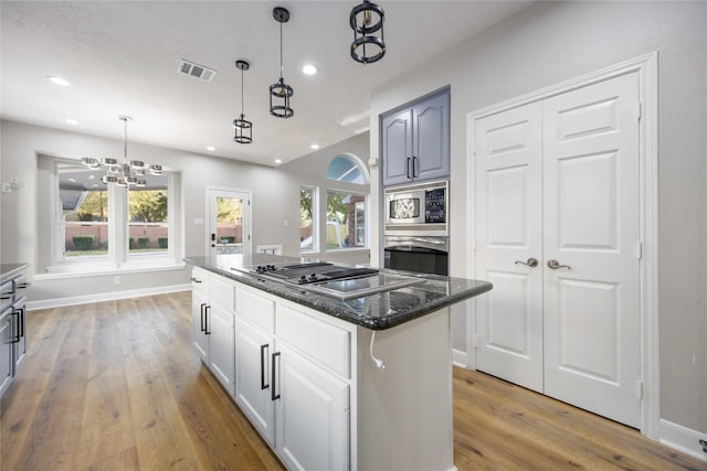 kitchen with a center island, stainless steel appliances, a chandelier, decorative light fixtures, and white cabinets